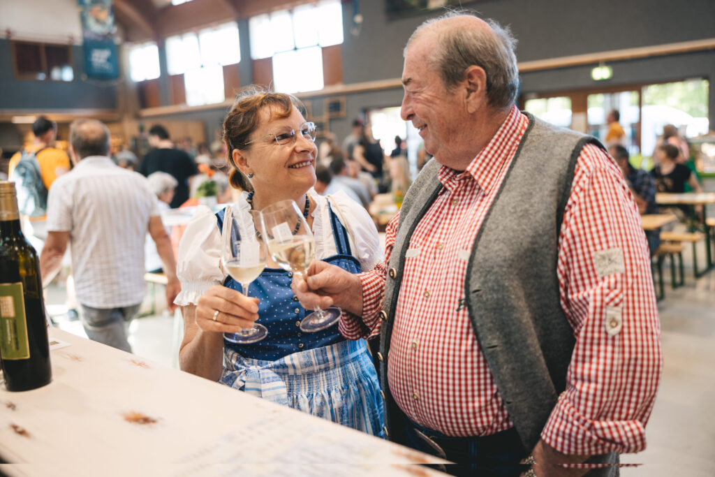 Ein älteres Paar in Tracht stoßt mit einem Glas Wein in der Festhalle an